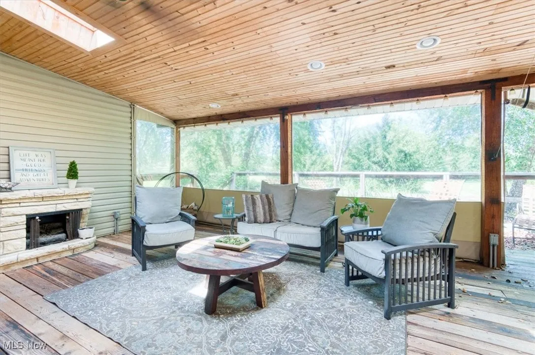 Sunroom with wooden ceiling, an outdoor living space with a fireplace, a skylight, a deck, and hardwood / wood-style floors