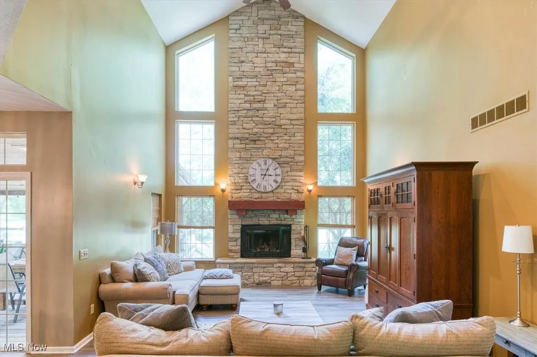 Living room with plenty of natural light, a stone fireplace, high vaulted ceiling, and wood finished floors