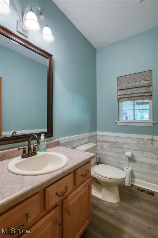Half bath with vanity, dark wood-type flooring, a textured ceiling, wainscoting, and tile walls