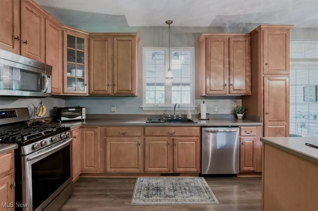 Kitchen with appliances with stainless steel finishes, brown cabinets, pendant lighting, and dark wood finished floors