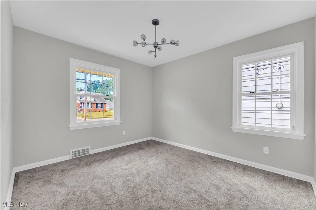 Carpeted empty room featuring baseboards and a chandelier
