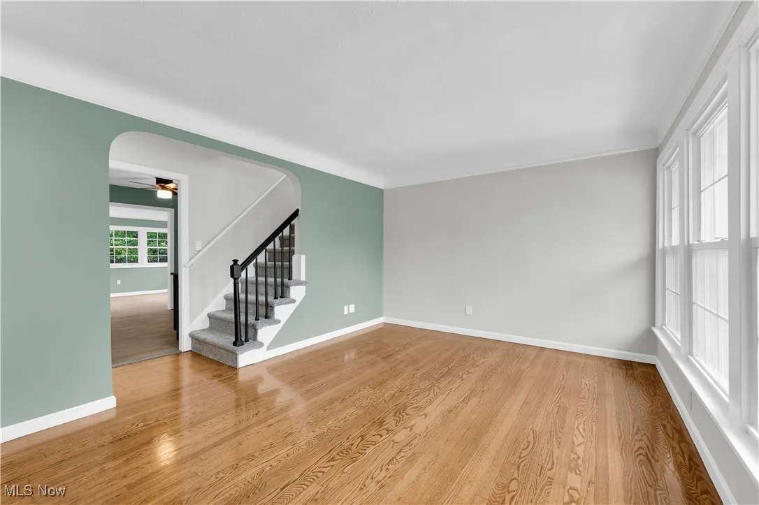 Empty room with stairway, light wood-style floors, a ceiling fan, and arched walkways