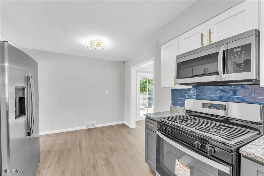 Kitchen with appliances with stainless steel finishes, light stone counters, light wood-style flooring, and white cabinetry