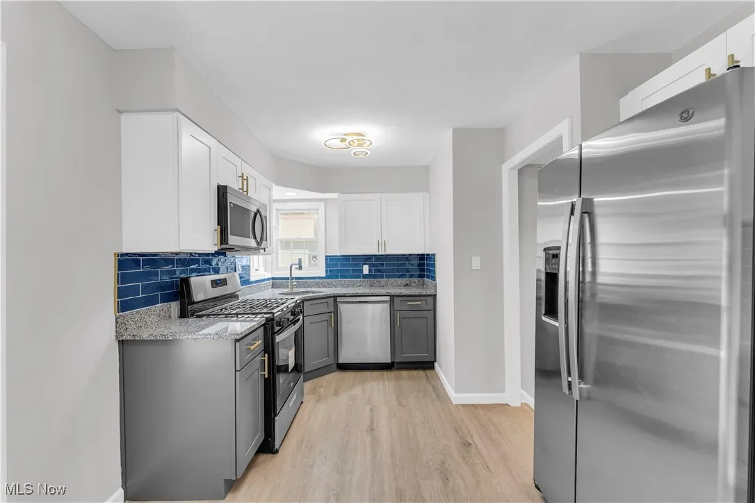 Kitchen with stainless steel appliances, gray cabinets, light stone counters, and white cabinetry