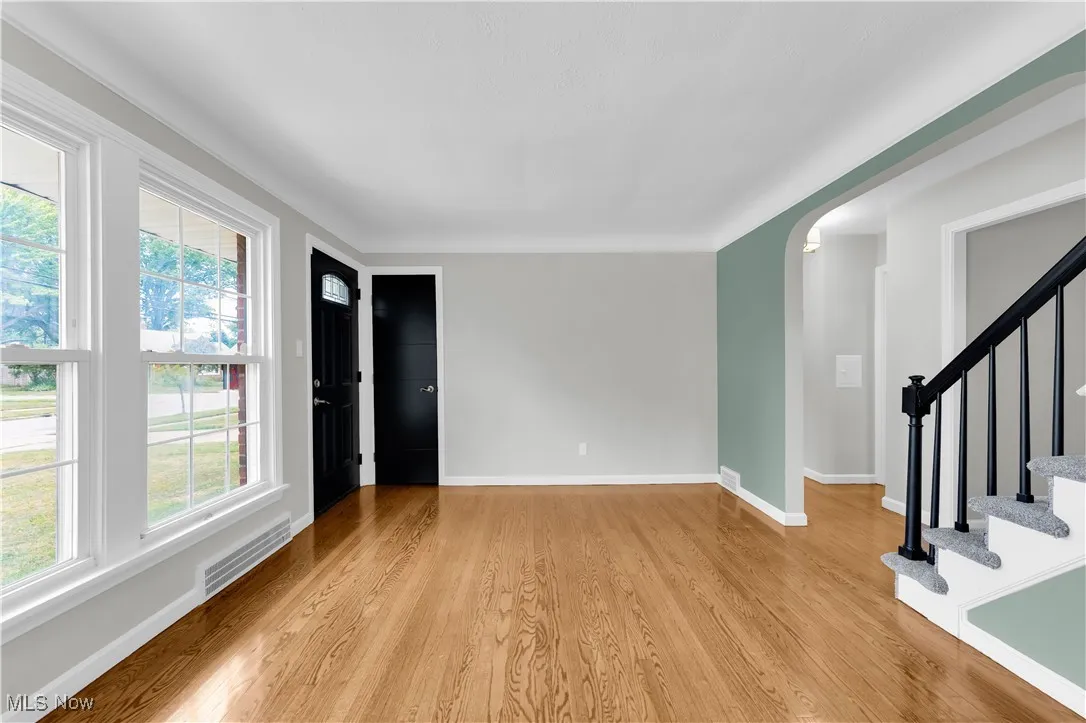 Empty room with stairs, light wood-style flooring, and arched walkways