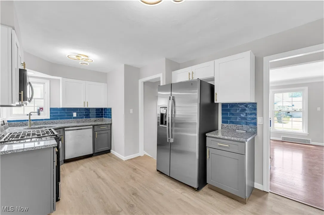 Kitchen featuring gray cabinets, appliances with stainless steel finishes, light stone counters, tasteful backsplash, and light wood-style flooring