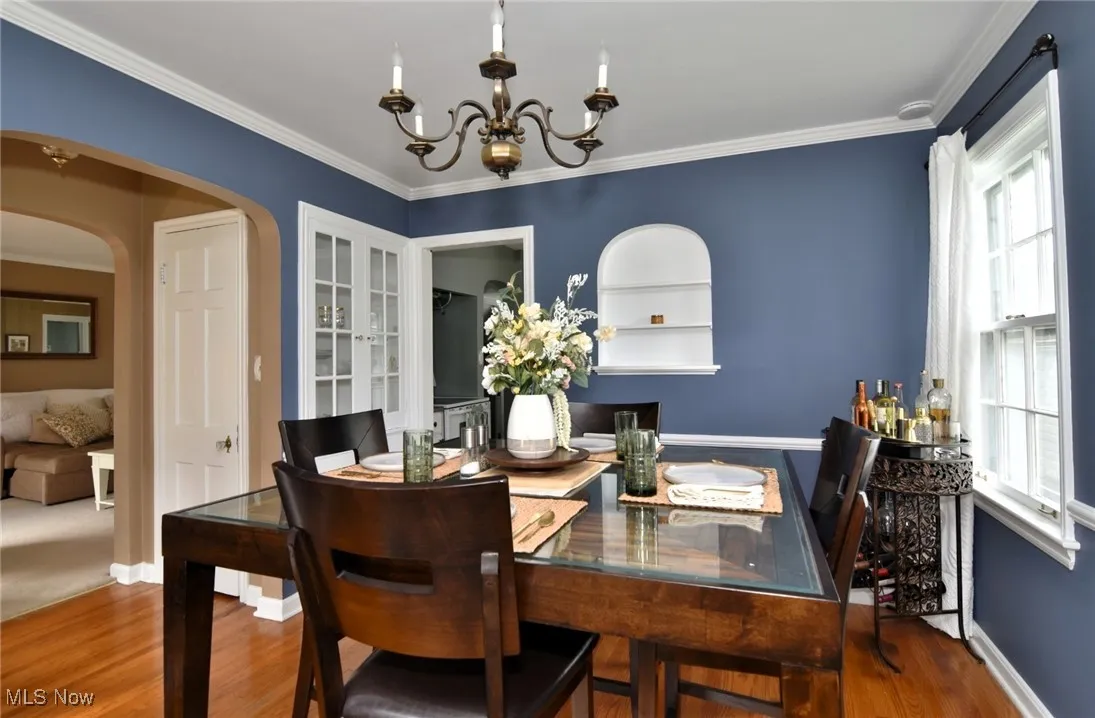 Dining room featuring crown molding, built in features, wood finished floors, arched walkways, and a chandelier