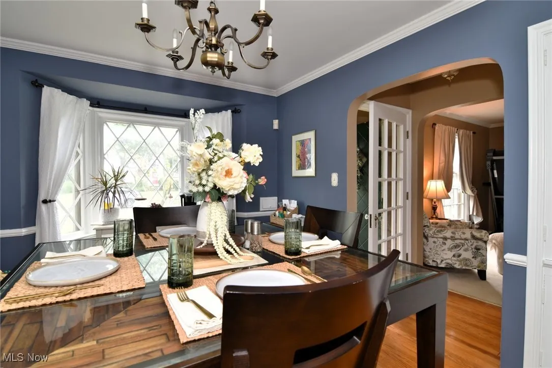 Dining area with crown molding, arched walkways, wood finished floors, and a chandelier
