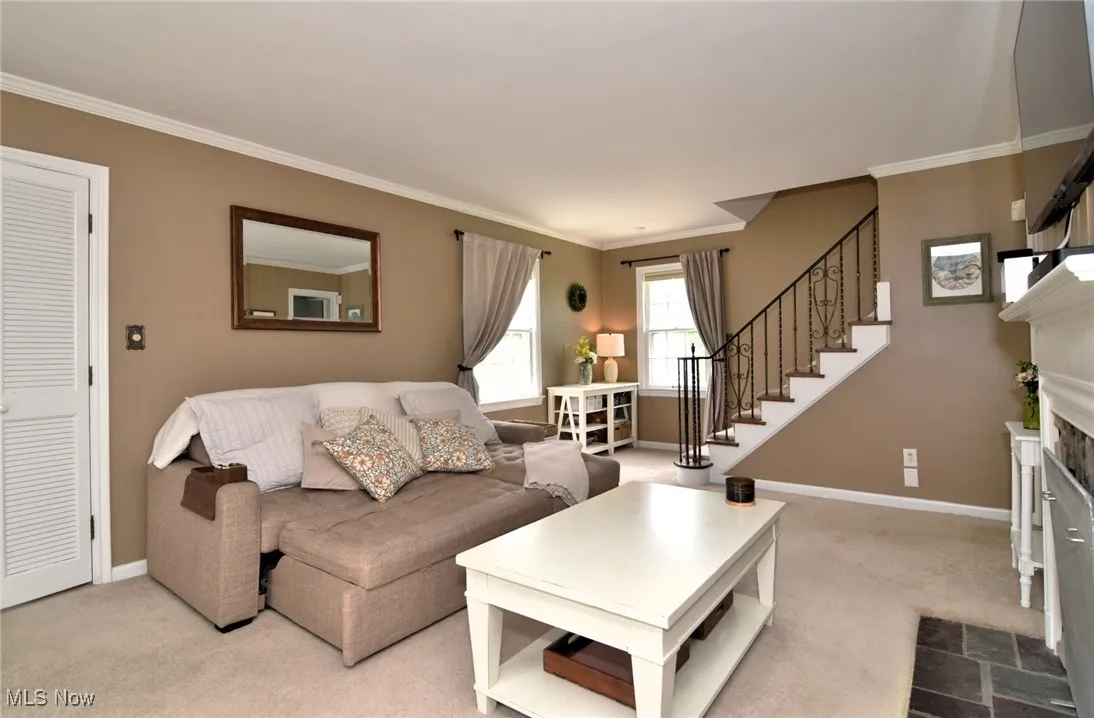 Carpeted living room with crown molding, stairway, and a premium fireplace