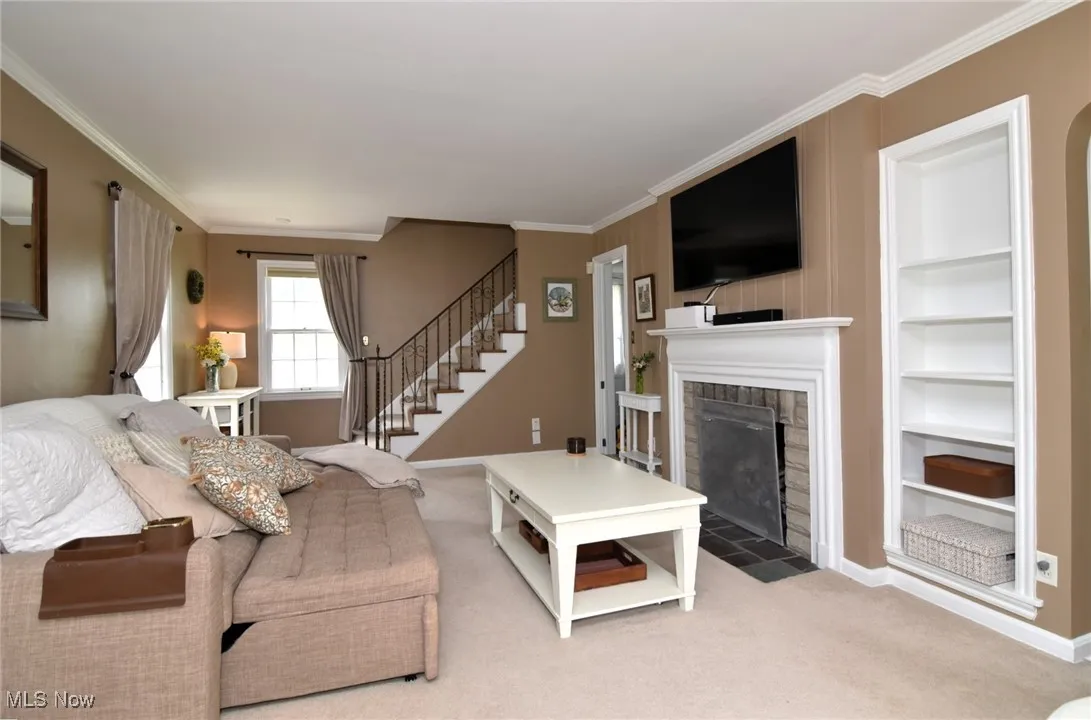 Living room featuring crown molding, a fireplace with flush hearth, carpet floors, stairs, and built in features