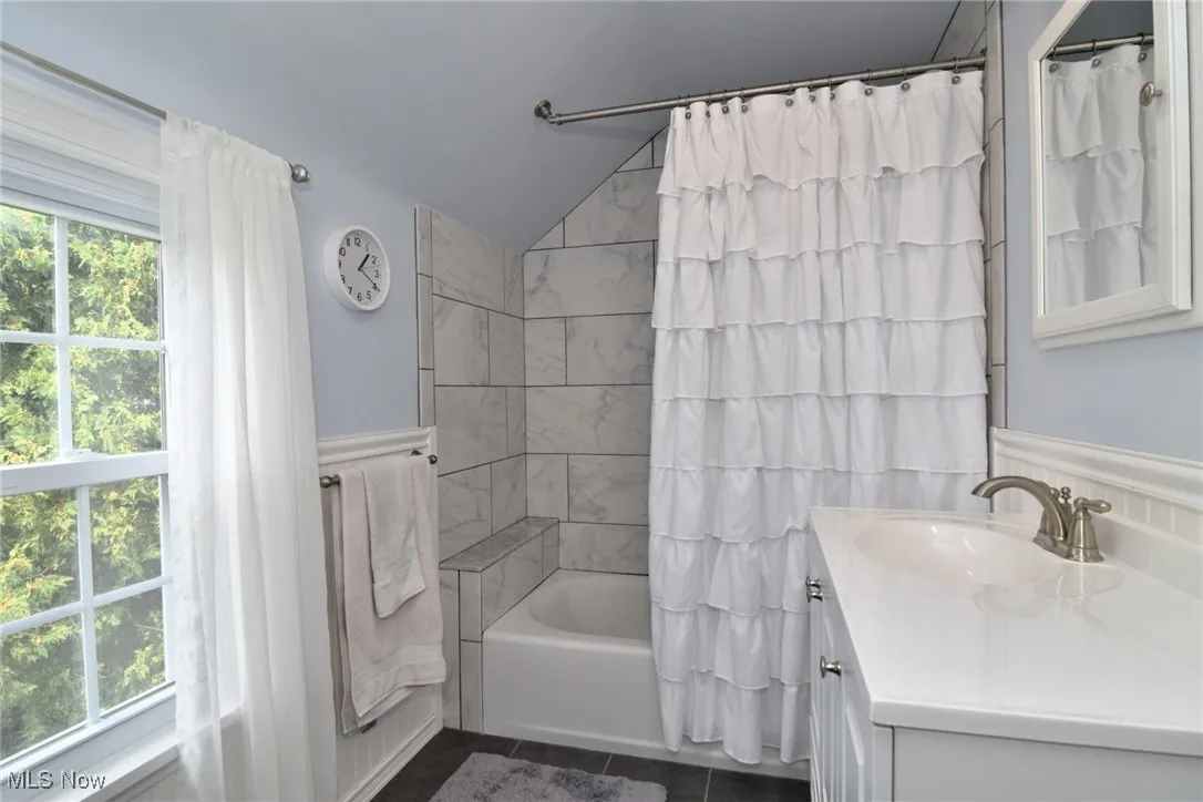 Full bath with vanity, shower / bath combination with curtain, lofted ceiling, and dark tile patterned flooring