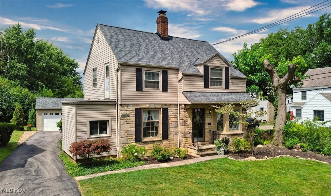 View of front facade with stone siding, an outbuilding, a chimney, a front lawn, and roof with shingles