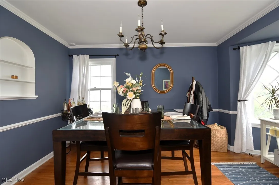 Dining space with wood finished floors, a chandelier, and ornamental molding