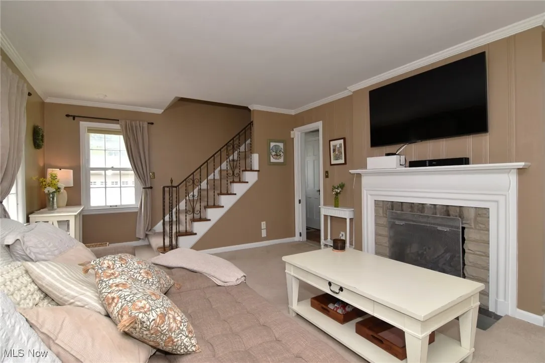 Carpeted living room featuring crown molding, a fireplace, and stairs