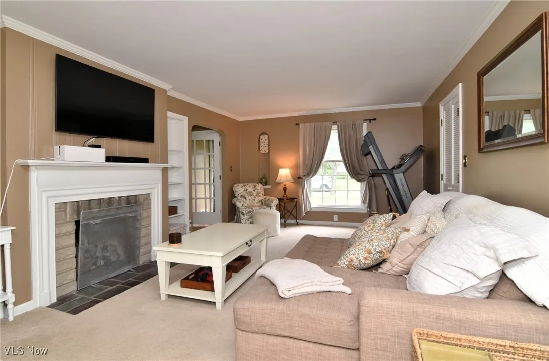 Living room featuring carpet floors, ornamental molding, a fireplace with flush hearth, and arched walkways