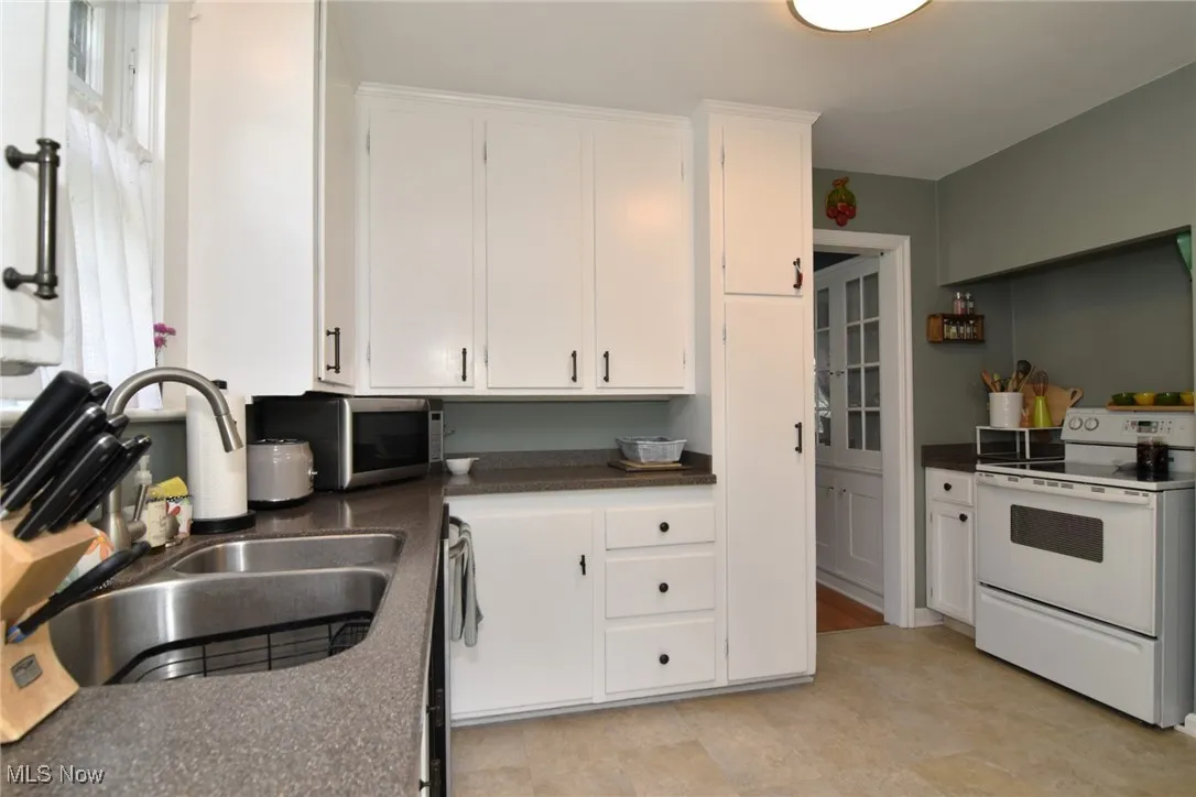 Kitchen with white electric range oven, white cabinets, and stainless steel microwave