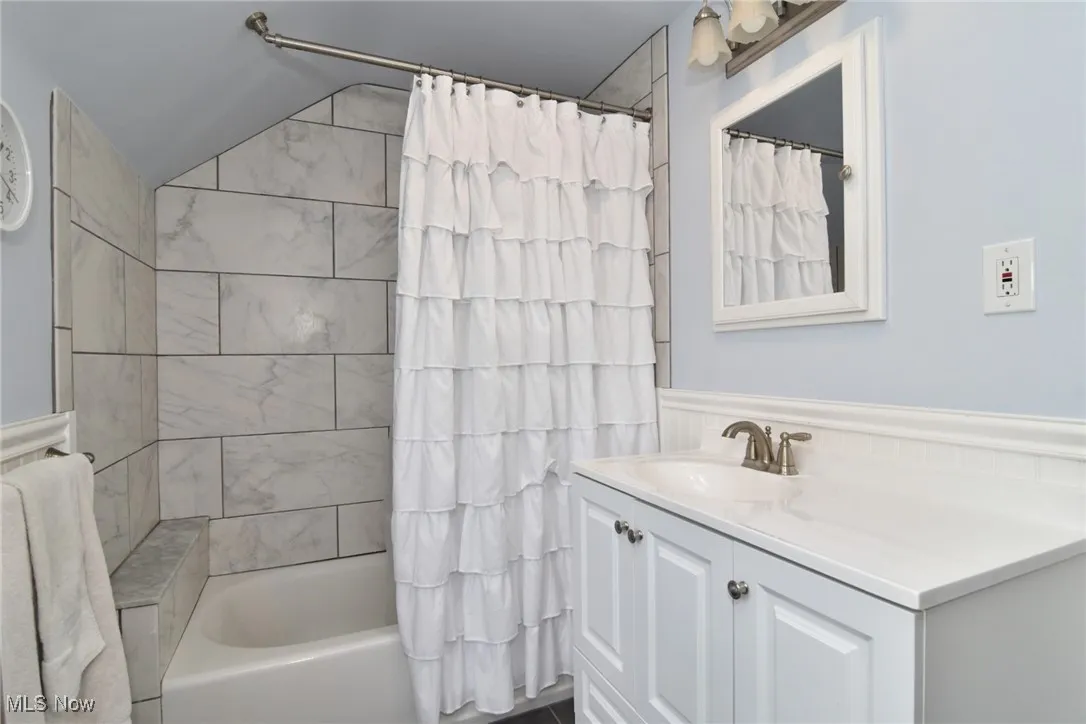 Bathroom with vanity, shower / bath combo with shower curtain, and vaulted ceiling