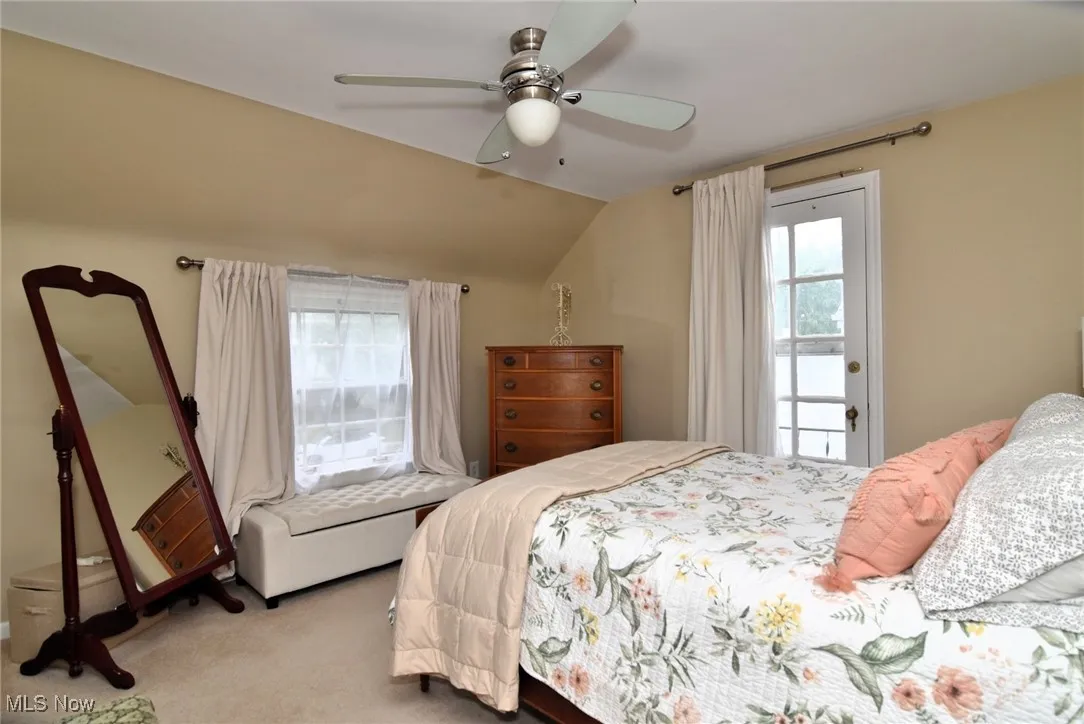 Carpeted bedroom with vaulted ceiling, multiple windows, and a ceiling fan
