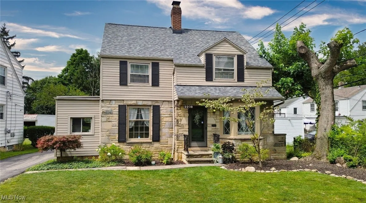 View of front of home featuring a shingled roof, a front lawn, stone siding, and a chimney