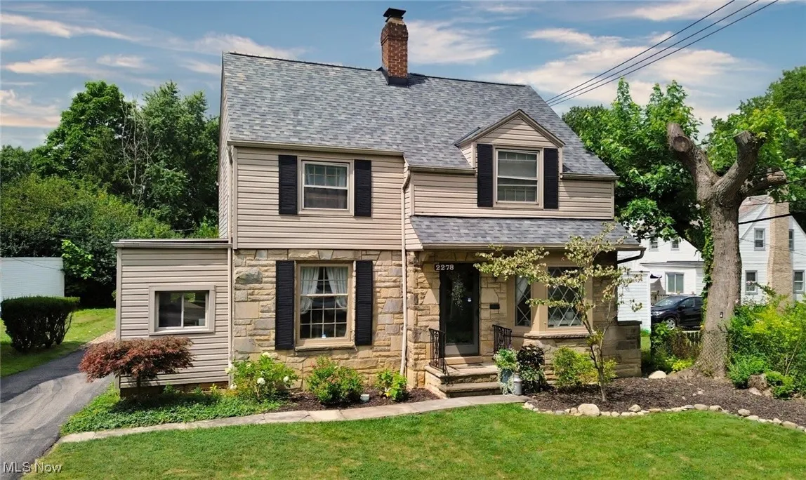 View of front of home featuring a shingled roof, a front yard, stone siding, and a chimney