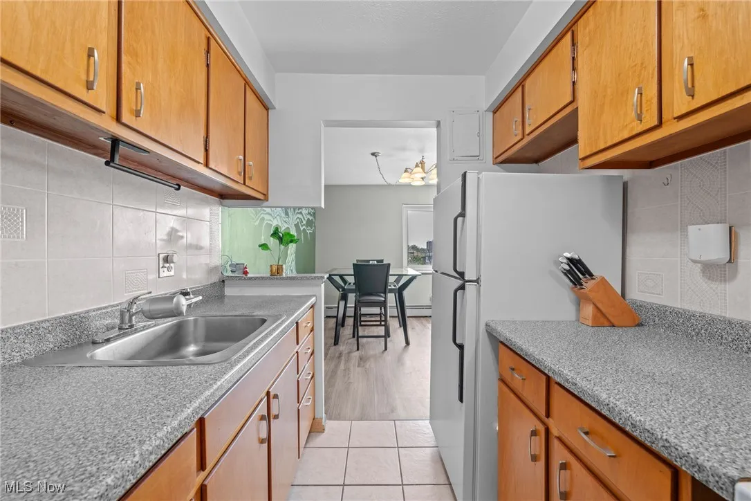 Kitchen featuring decorative backsplash, freestanding refrigerator, and brown cabinetry