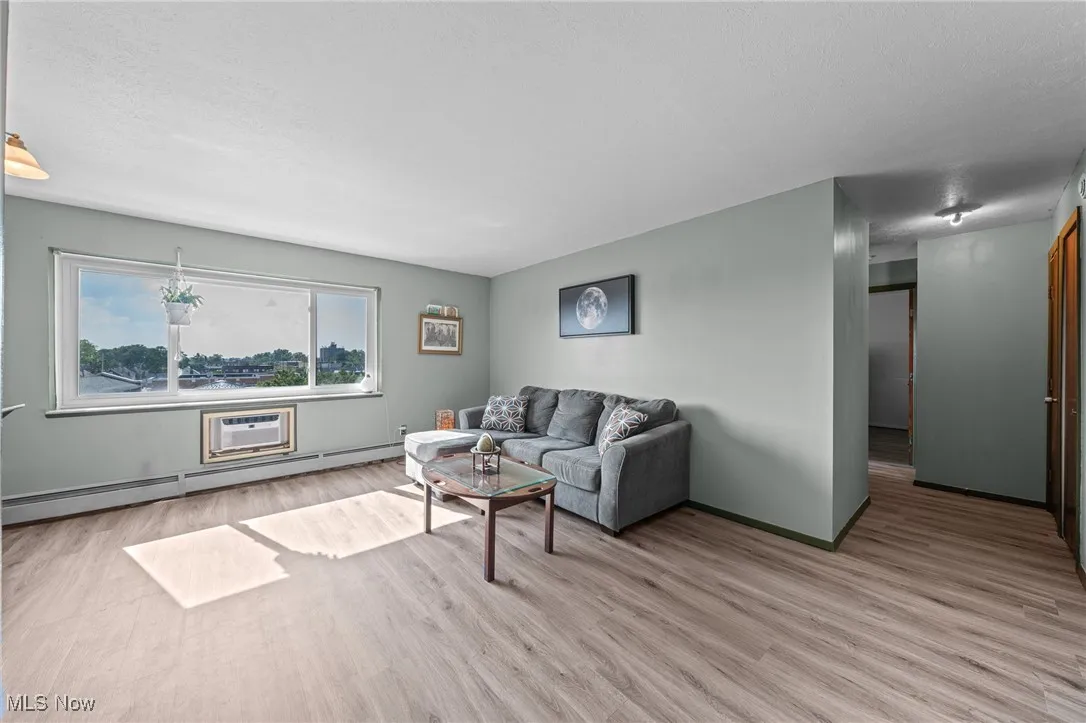 Living area featuring light wood-style flooring, a baseboard heating unit, and a textured ceiling