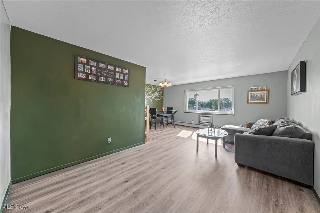 Living room with wood finished floors, a chandelier, a textured ceiling, and baseboard heating