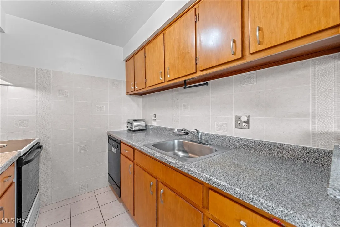 Kitchen featuring light tile patterned floors, tile walls, electric stove, brown cabinetry, and black dishwasher