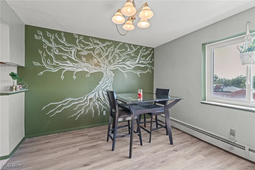 Dining space featuring an accent wall, light wood finished floors, a chandelier, and a baseboard radiator