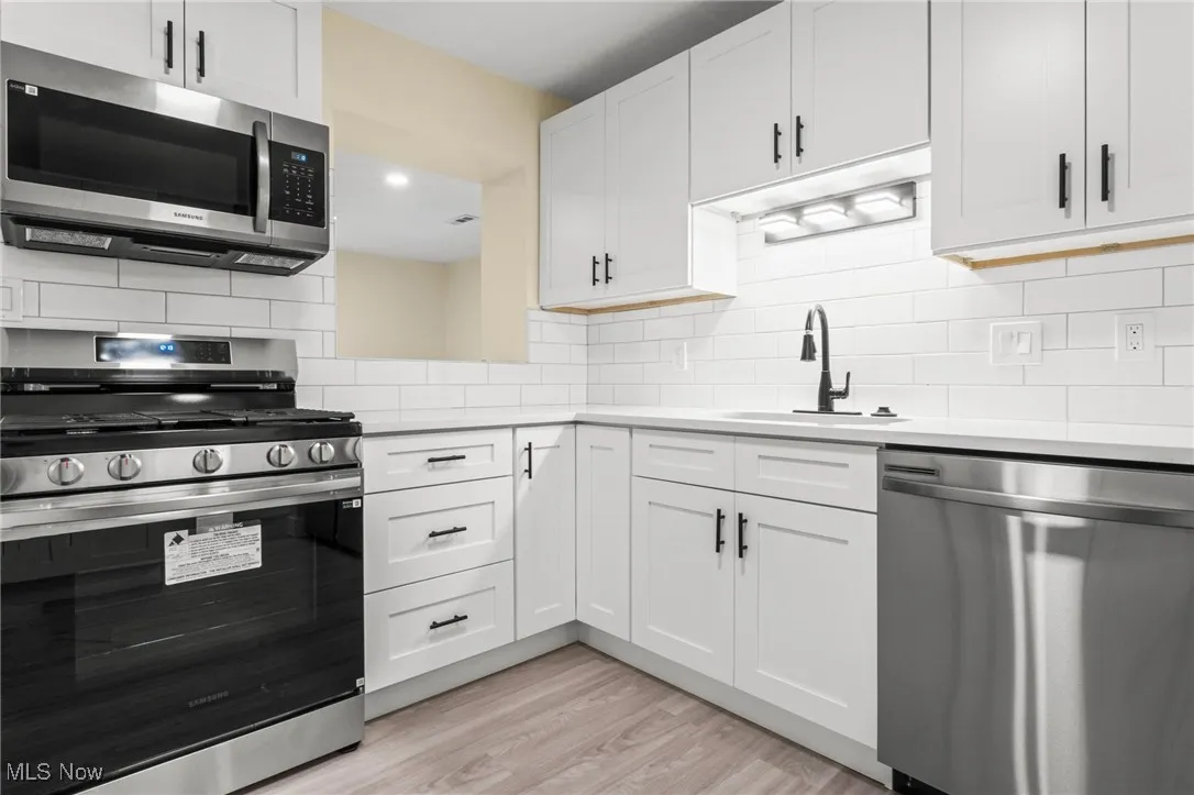 Kitchen featuring appliances with stainless steel finishes, decorative backsplash, light countertops, light wood finished floors, and white cabinetry