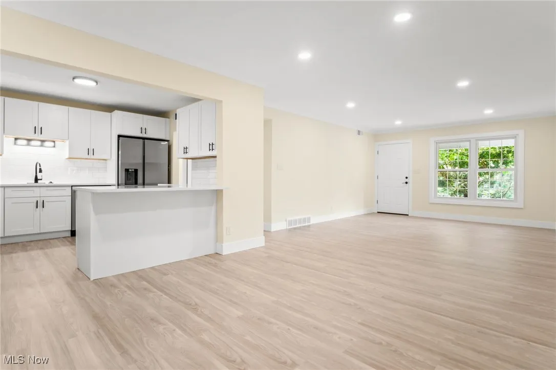 Kitchen featuring recessed lighting, stainless steel refrigerator with ice dispenser, open floor plan, light wood-type flooring, and decorative backsplash