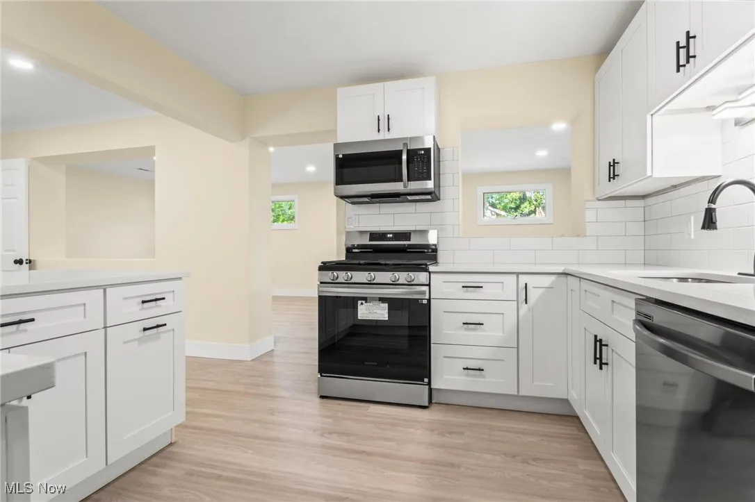 Kitchen with appliances with stainless steel finishes, white cabinetry, light wood finished floors, decorative backsplash, and light countertops