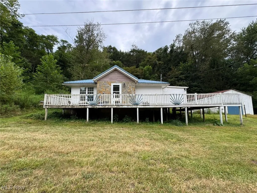 View of front facade featuring a wooden deck, a metal roof, and a front yard