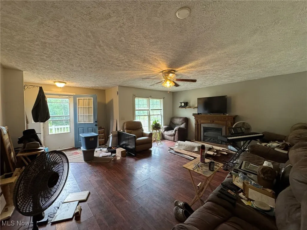 Living area featuring a fireplace, a textured ceiling, wood finished floors, and ceiling fan