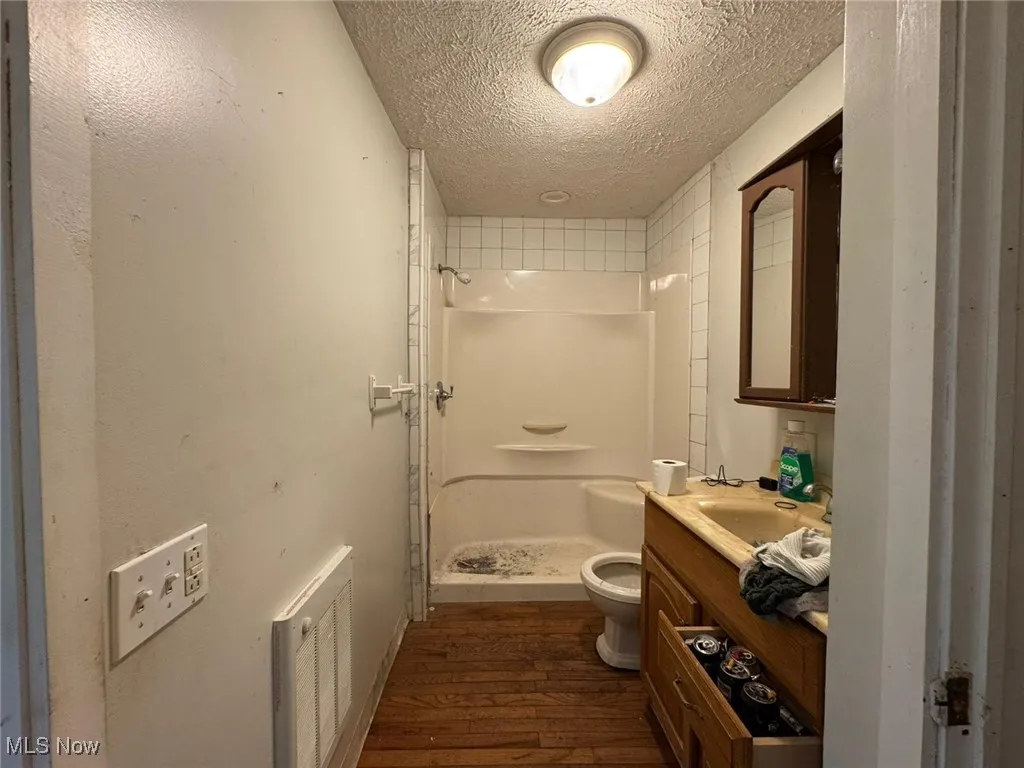 Bathroom featuring a textured ceiling, dark wood-style floors, vanity, and a stall shower