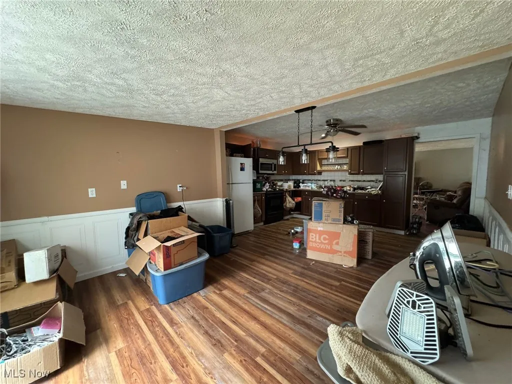 Living room featuring a wainscoted wall, dark wood-style floors, a textured ceiling, a decorative wall, and a ceiling fan