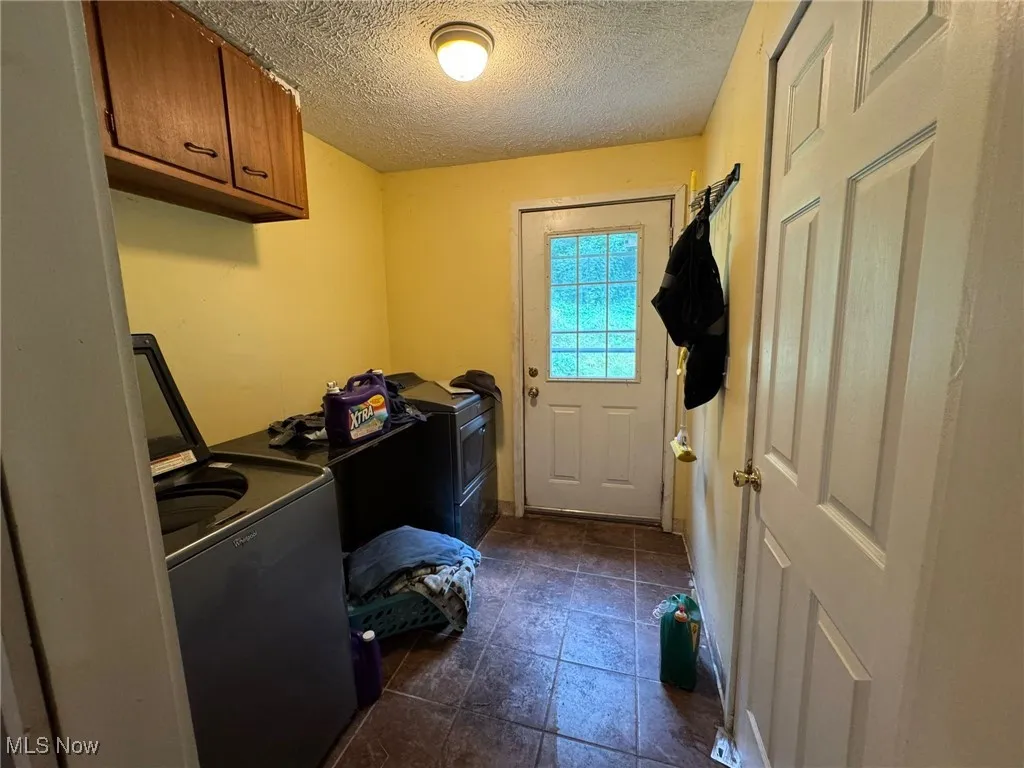 Laundry area with a textured ceiling, washer and clothes dryer, cabinet space, and dark tile patterned floors