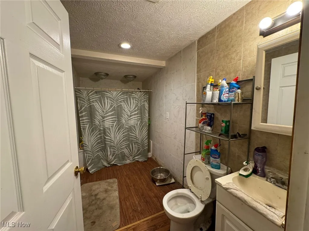 Full bath featuring dark wood finished floors, vanity, tile walls, and a textured ceiling