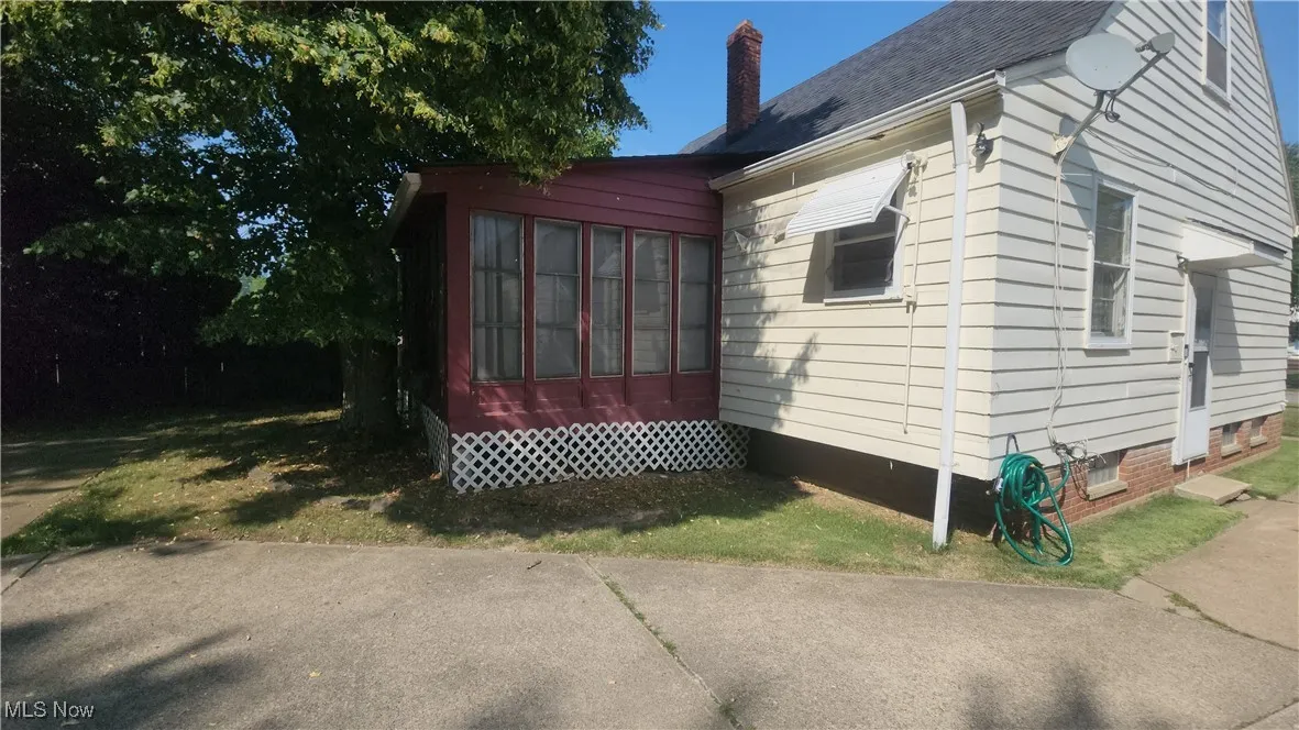 View of side of property featuring crawl space, a chimney, roof with shingles, and a sunroom