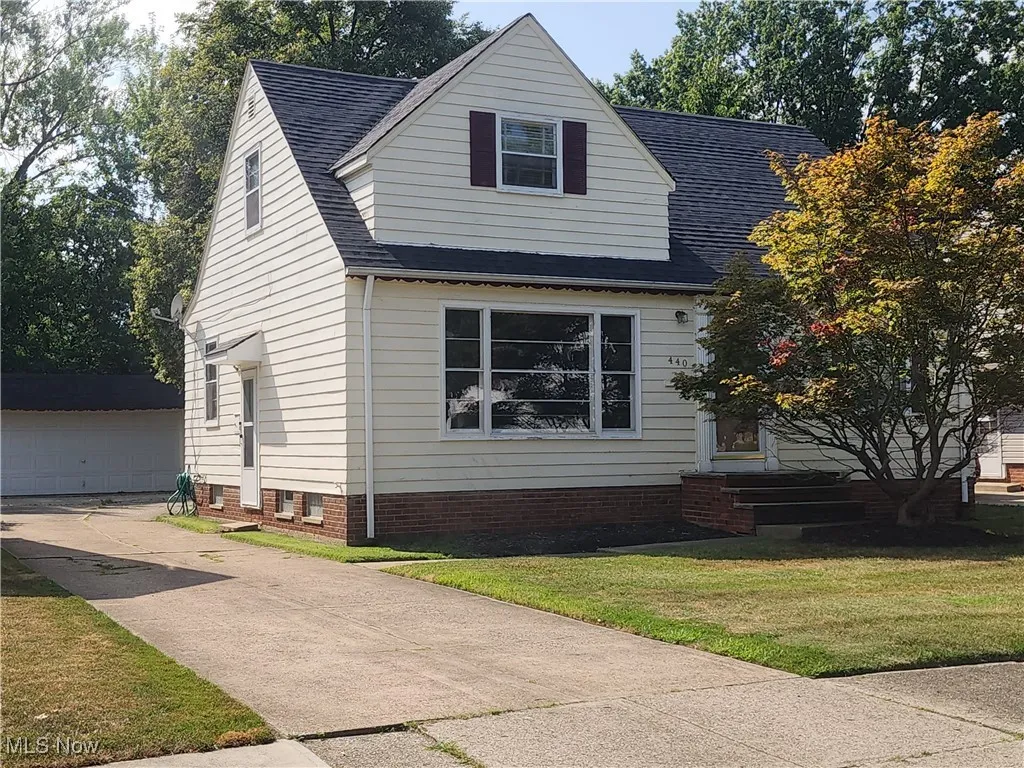 View of front facade with roof with shingles, a detached garage, an outbuilding, and a front yard