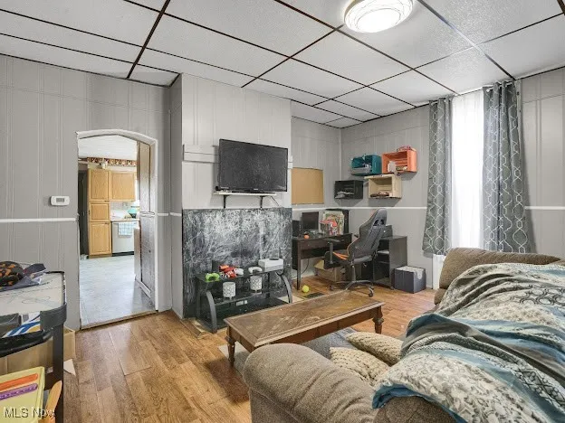 Living area featuring a drop ceiling, wood finished floors, arched walkways, and an office area