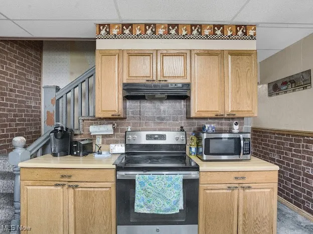 Kitchen with brick wall, stainless steel appliances, light countertops, a paneled ceiling, and extractor fan