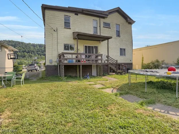 Rear view of property featuring a wooden deck, stairway, and a trampoline