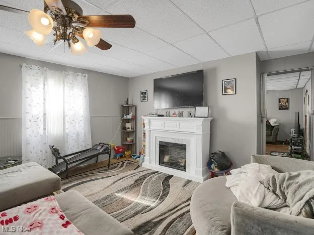 Living area with a drop ceiling, a glass covered fireplace, and a ceiling fan