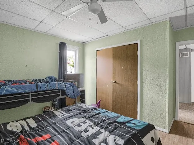 Bedroom featuring a textured wall, wood finished floors, a drop ceiling, a closet, and a ceiling fan