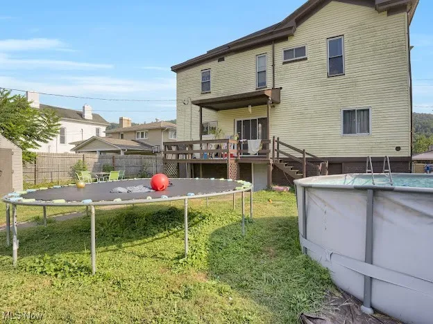Rear view of house featuring an outdoor pool, a trampoline, stairway, and a deck