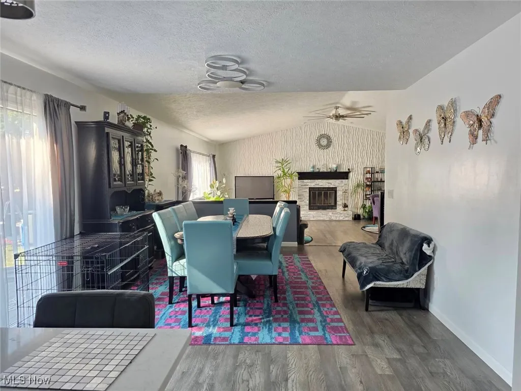 Dining space with lofted ceiling, wood finished floors, a textured ceiling, and a glass covered fireplace
