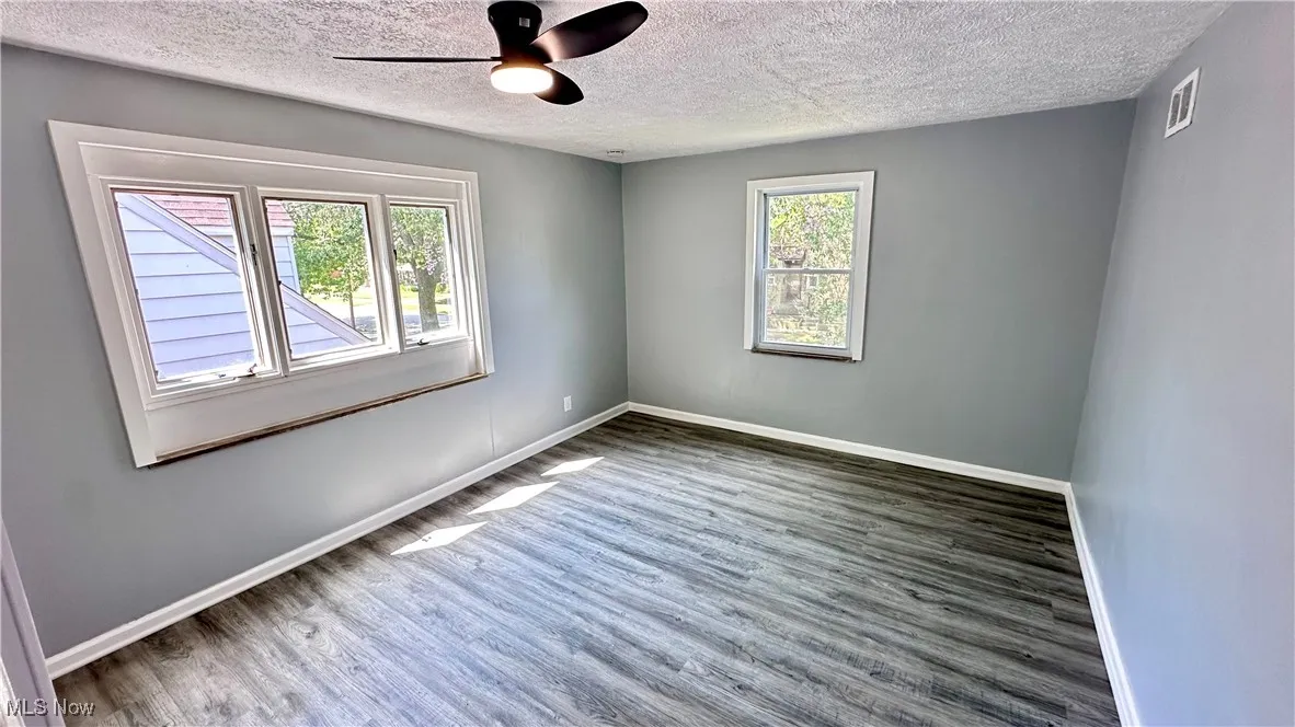 Empty room with wood finished floors, ceiling fan, and a textured ceiling