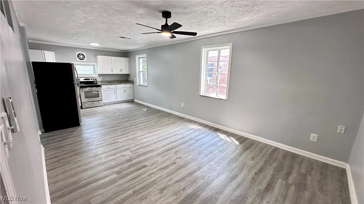 Kitchen featuring stainless steel appliances, white cabinets, a textured ceiling, light wood-type flooring, and a ceiling fan