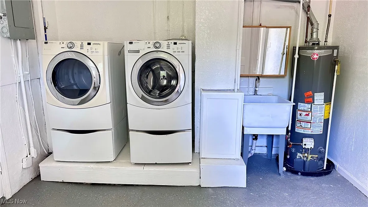 Washroom with gas water heater, washing machine and dryer, a textured wall, and electric panel